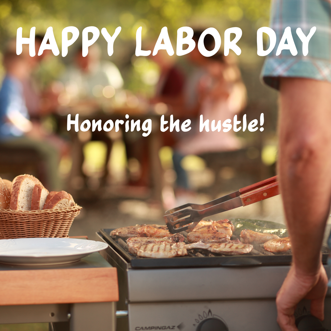 Outdoor Labor Day cookout with someone grilling while people gather at a picnic table in a sunny park.
