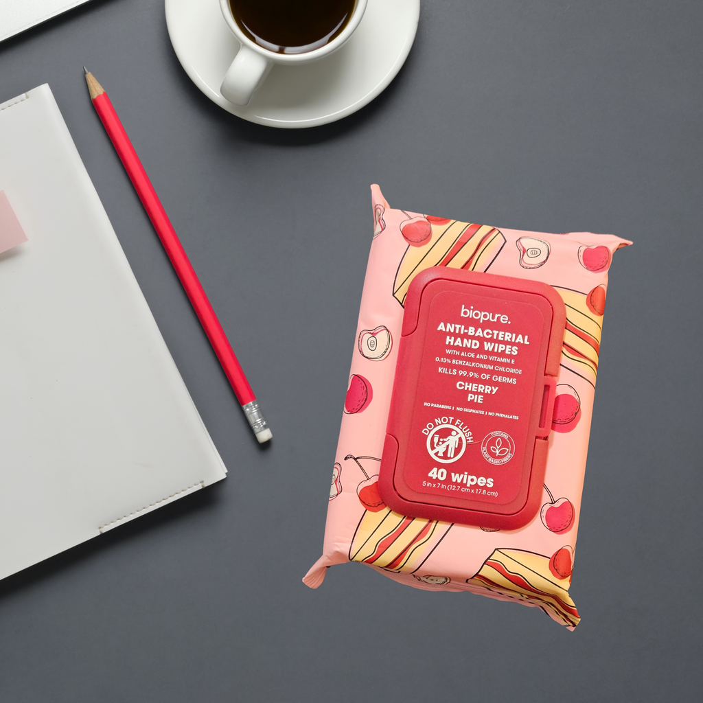 A package of biopure. Anti-Bacterial Hand Wipes in Cherry Pie scent, styled on a dark gray desk next to a red pencil, a white notebook, and a cup of coffee.