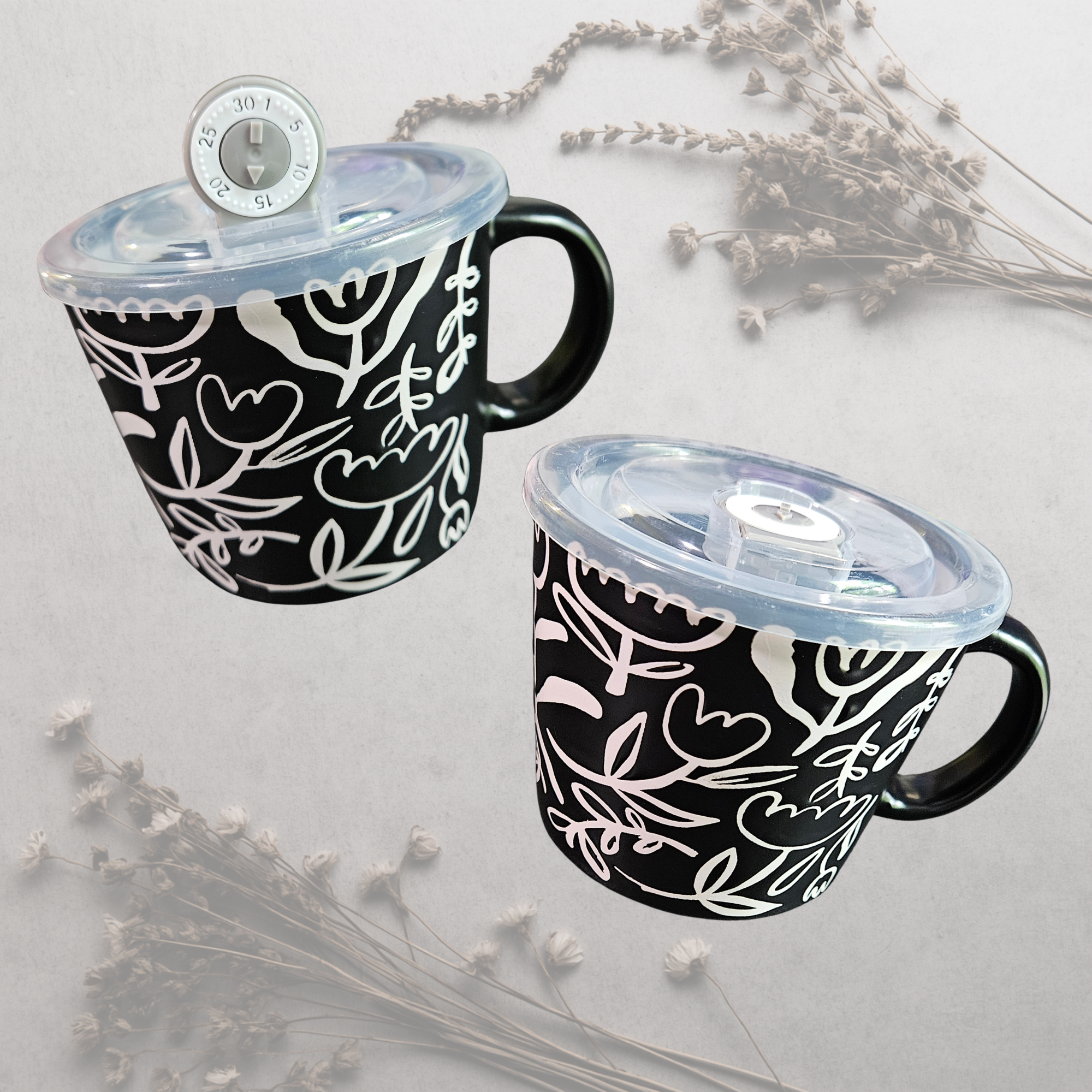 A ceramic soup mug with a modern floral design and a silicone‑sealed plastic lid featuring an adjustable dial and venting hole, available in black with white flowers or white with black flowers.