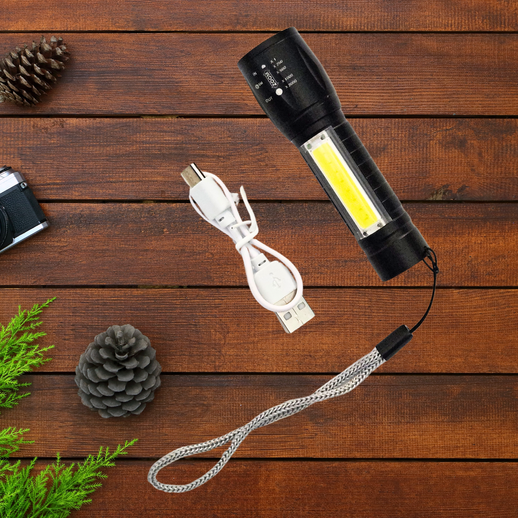 Mini flashlight with USB cable on a wooden surface with pine cones and a camera.
