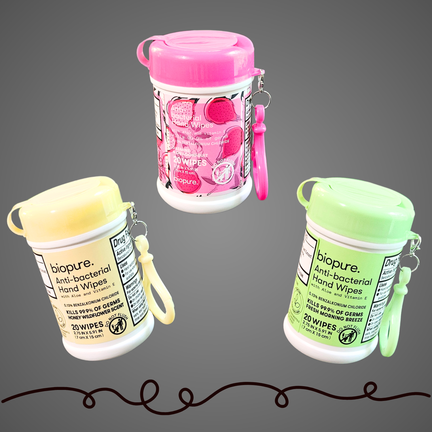 Three BioPure anti-bacterial hand wipe containers with pink, yellow, and green lids suspended against a gray background, each featuring a matching clip and labeled with their respective scents.