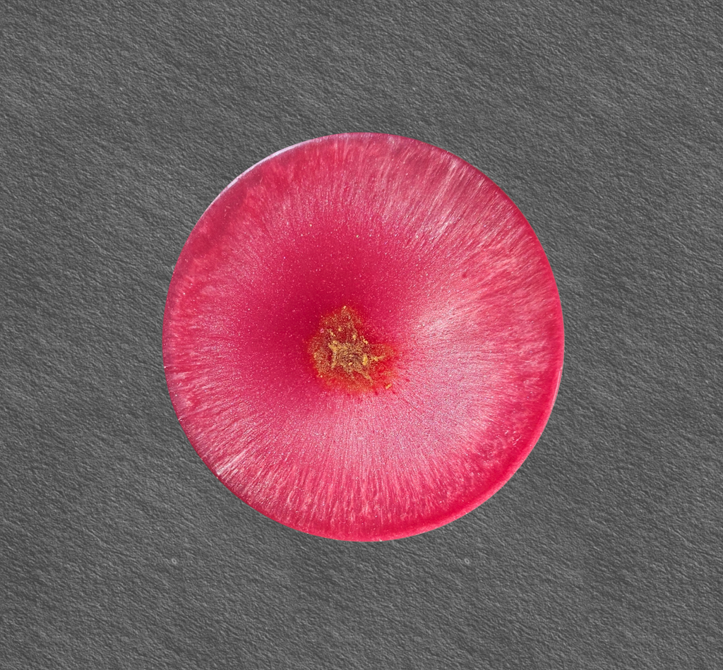 Handmade pink resin coaster with radiant crystal‑burst patterns on a dark background.