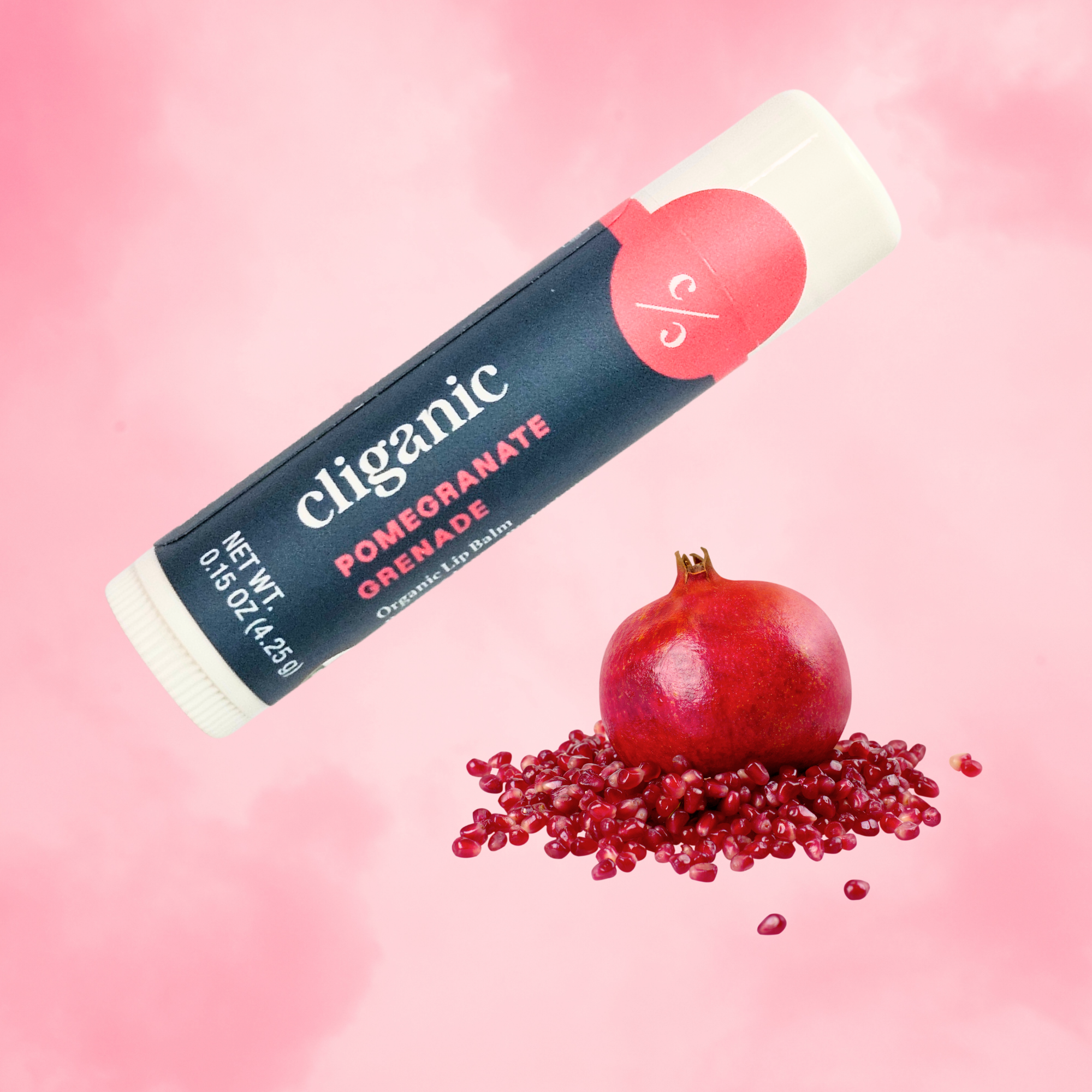 Cliganic Pomegranate organic lip balm tube on a soft pink background with a whole pomegranate and scattered seeds below.