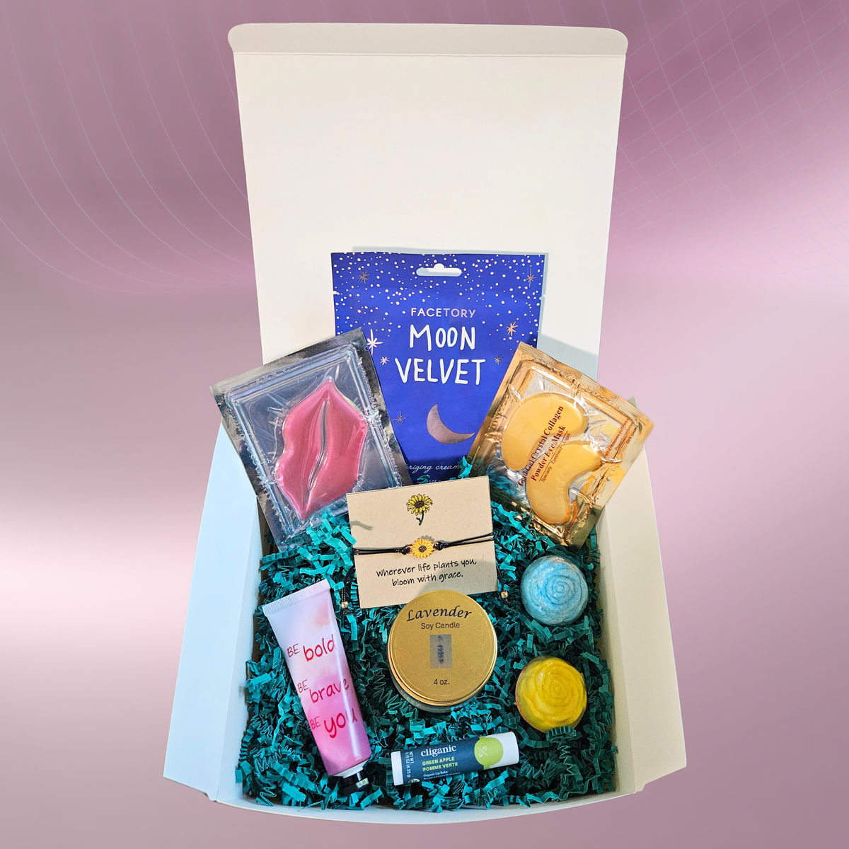 A self‑care gift box filled with items like face masks, a lip mask, eye mask, lavender candle, lip balm, bath bombs, and a sunflower bracelet arranged on teal filler against a pink‑purple background.