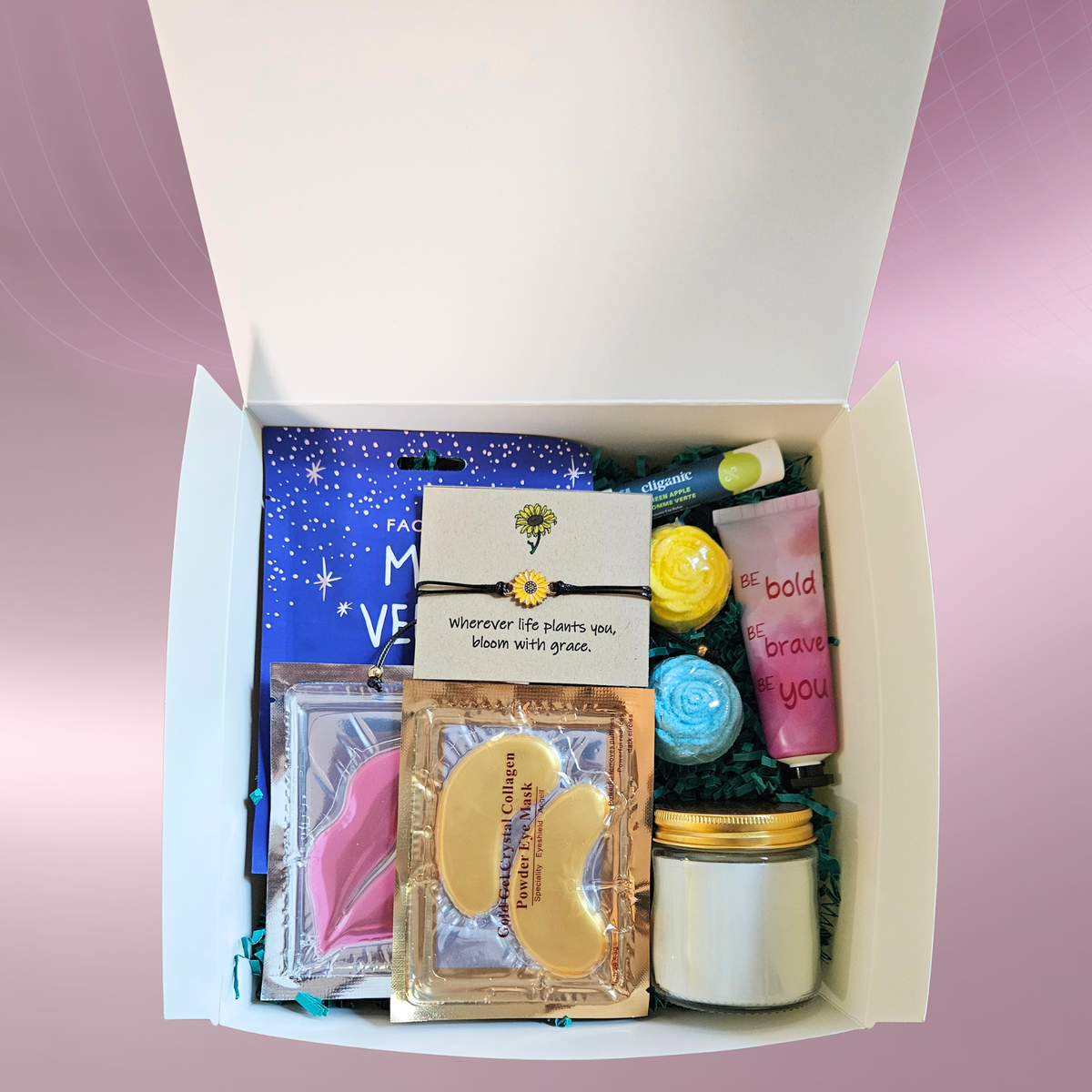 A flat lay of packed self‑care gift box filled with items like face masks, a lip mask, eye mask, lavender candle, lip balm, bath bombs, and a sunflower bracelet arranged on teal filler against a pink‑purple background.