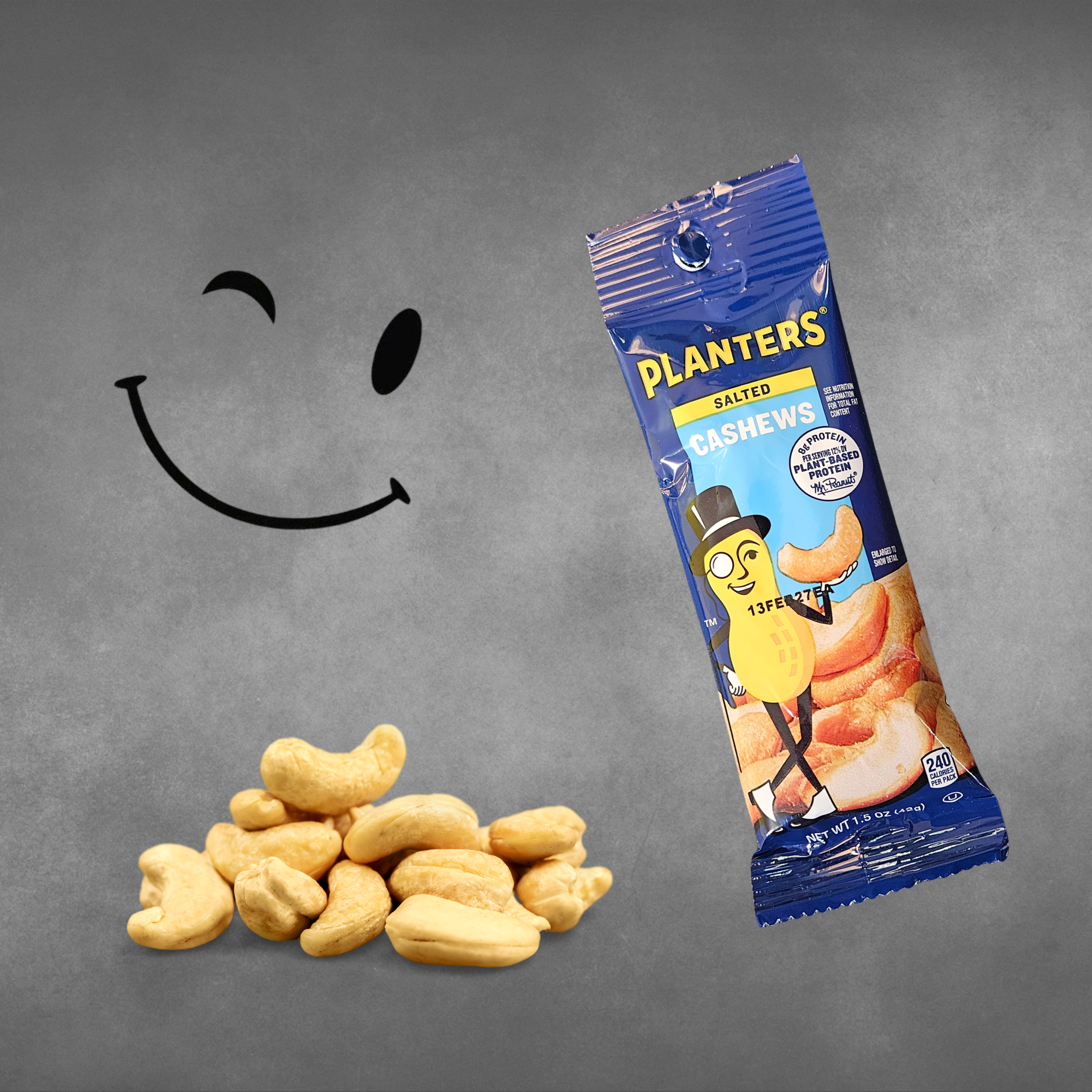 A package of Planters Salted Cashews snack is shown on a textured gray background next to a pile of cashews and a simple black smiley face graphic.
