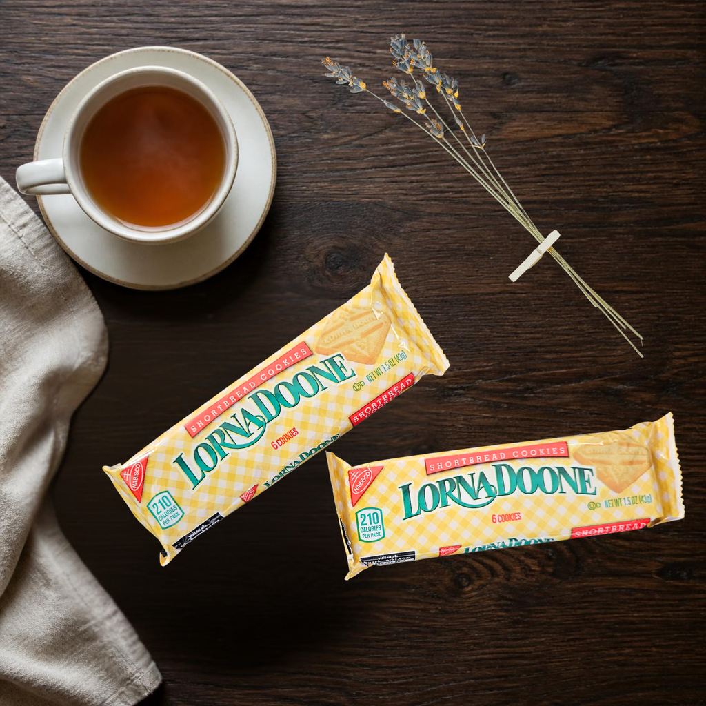 Two Lorna Doone shortbread cookie 6-packs in their signature yellow-and-white checkered wrapper are arranged on a dark wooden table next to a cup of tea and dried flowers.