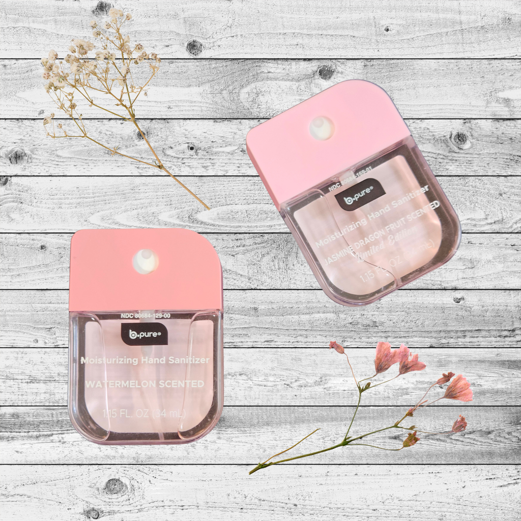 Two pink hand sanitizer pocket size spray bottles on a wooden surface with flowers.
