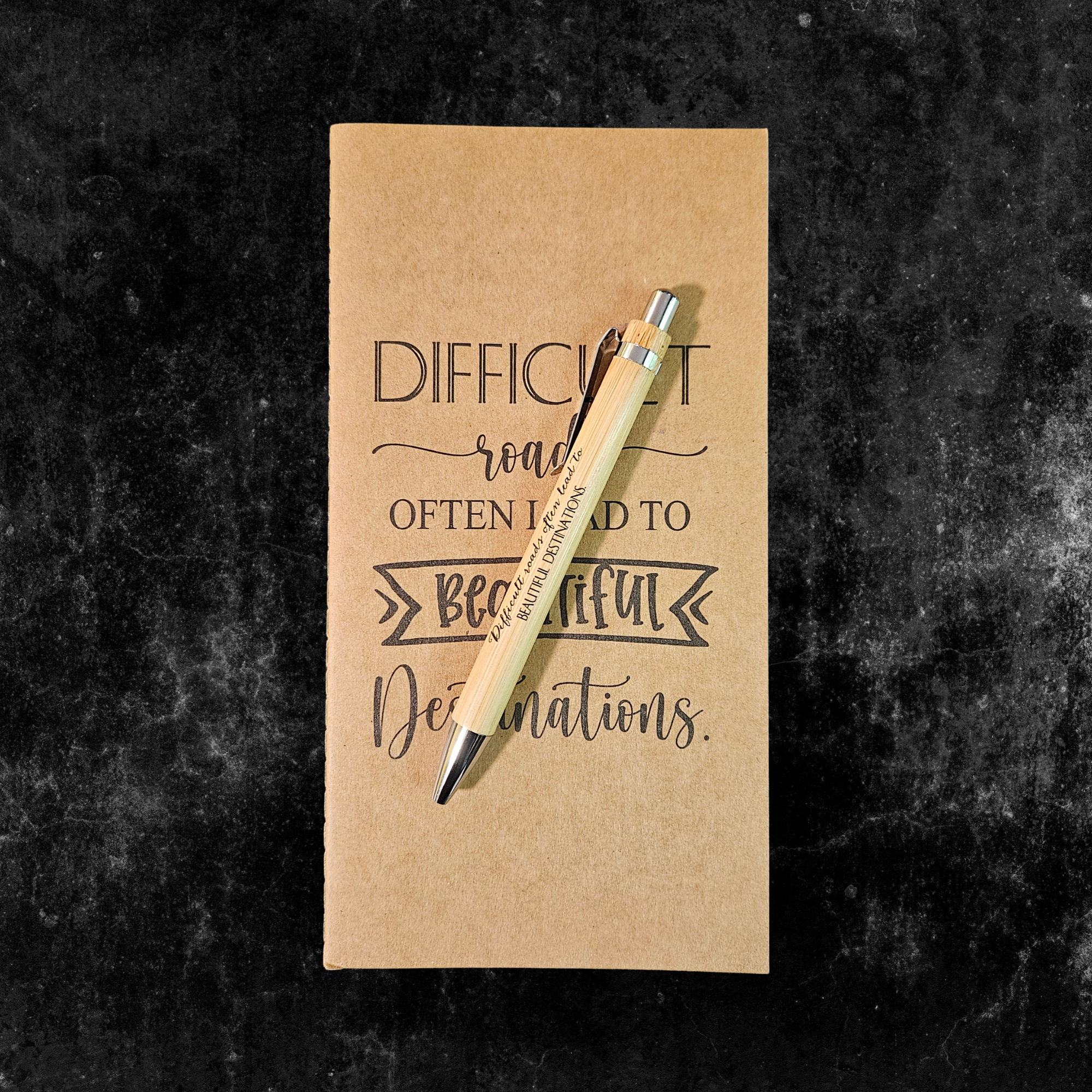 Kraft planner with motivational quote, Difficult roads often lead to beautify destinations, and pen on a dark textured background