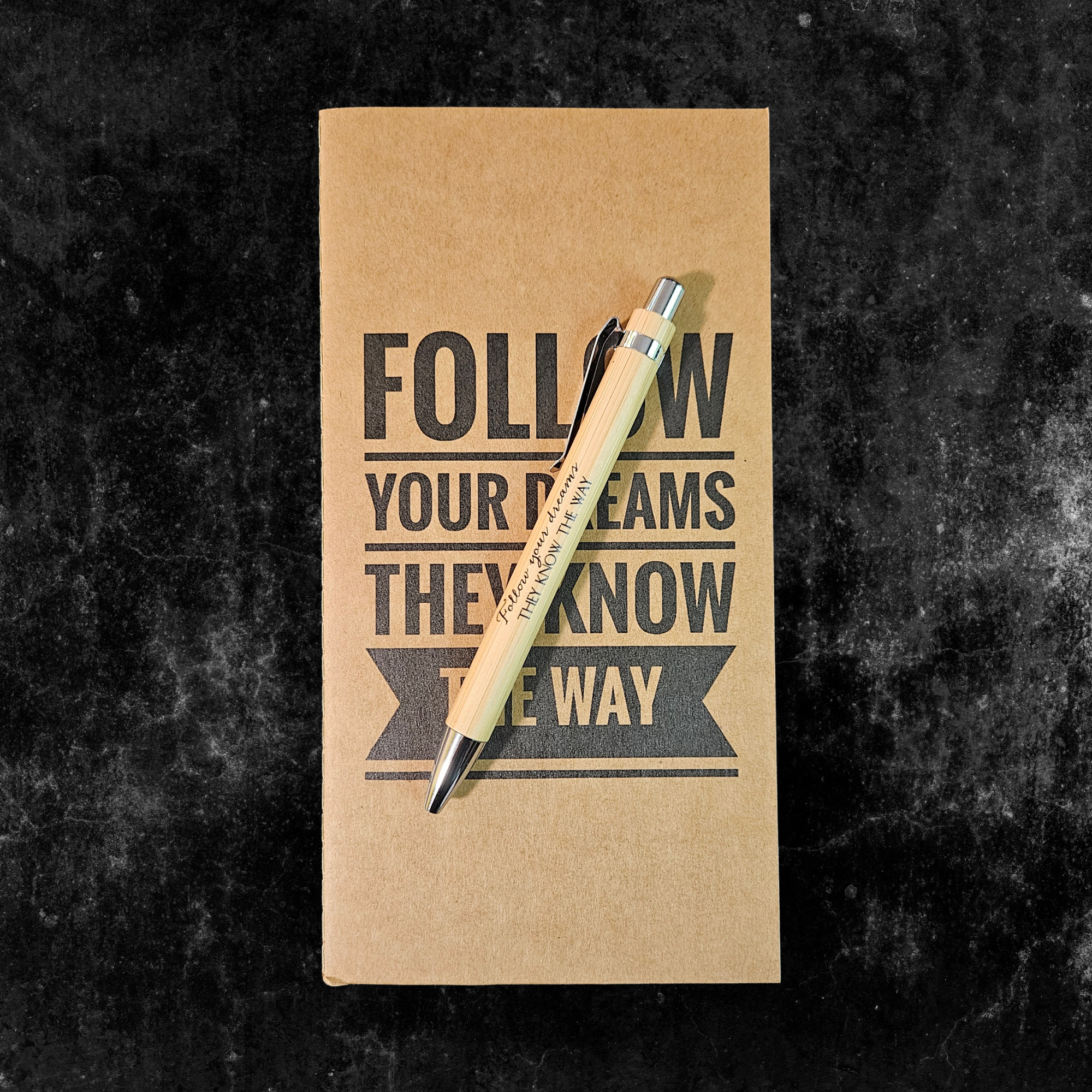 Kraft planner with motivational quote, Follow your dreams they know the way, and pen on a dark textured background