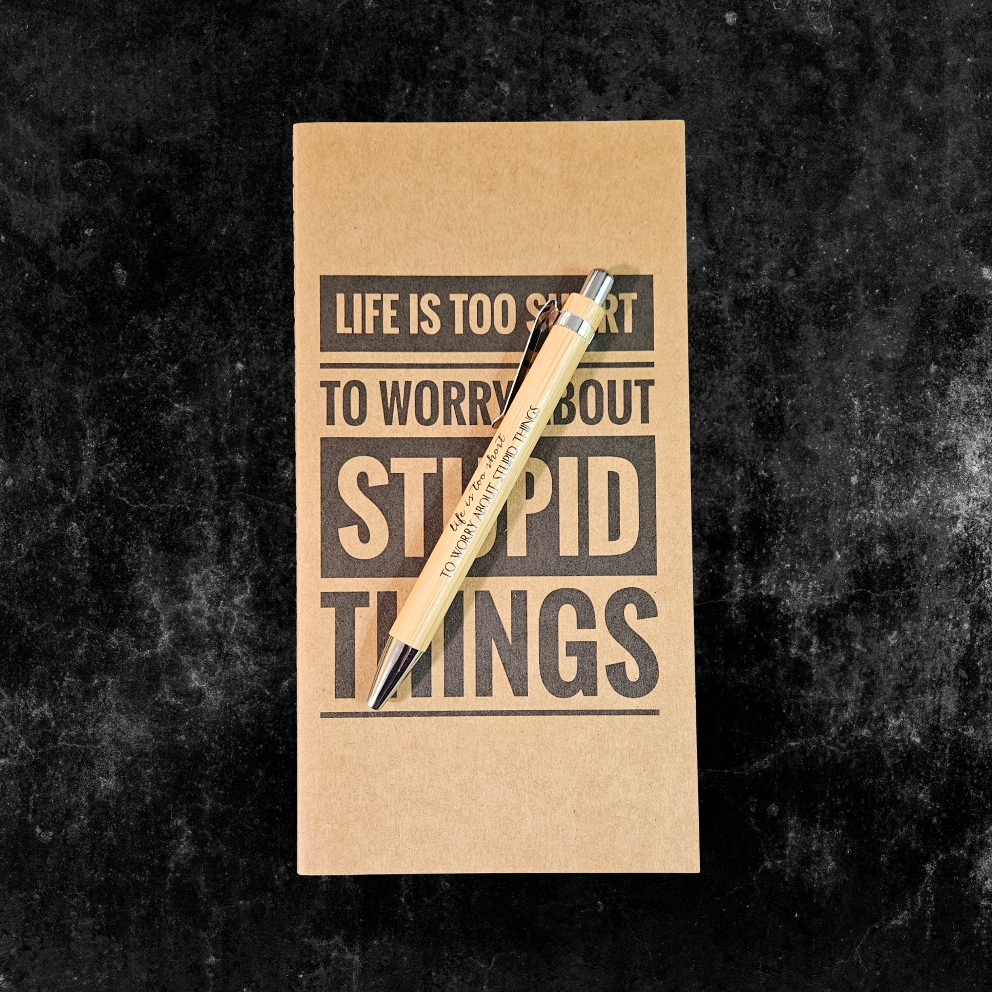 Kraft planner with motivational quote, Life is too short to worry about stupid things, and pen on a dark textured background