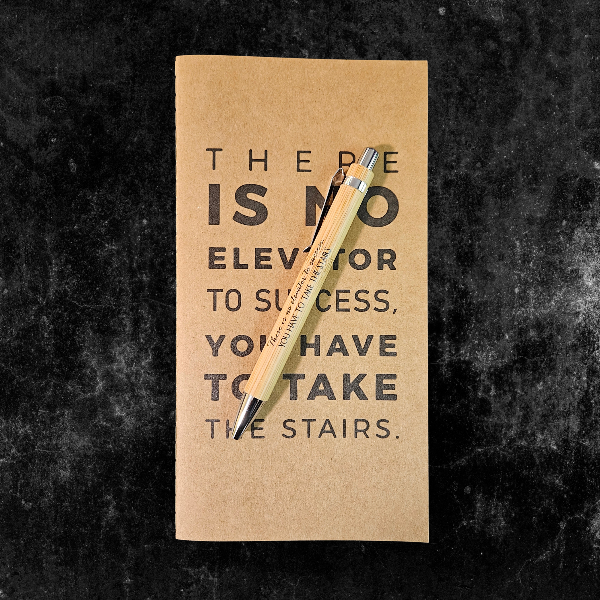 Kraft planner with motivational quote, There is no elevator to success you have to take the stairs, and pen on a dark textured background