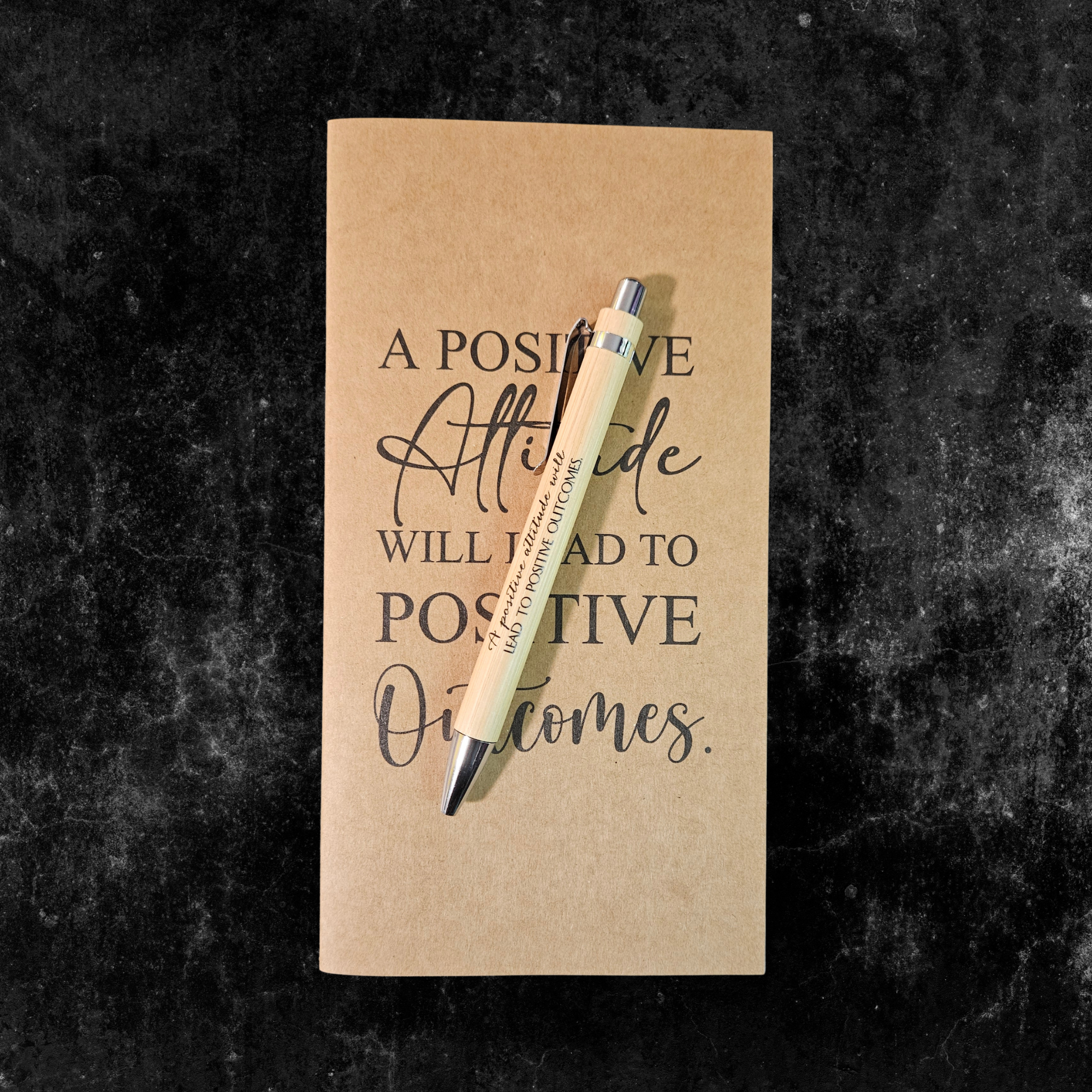 Kraft planner with motivational quote, A positive attitude will lead to positive outcomes, and pen on a dark textured background