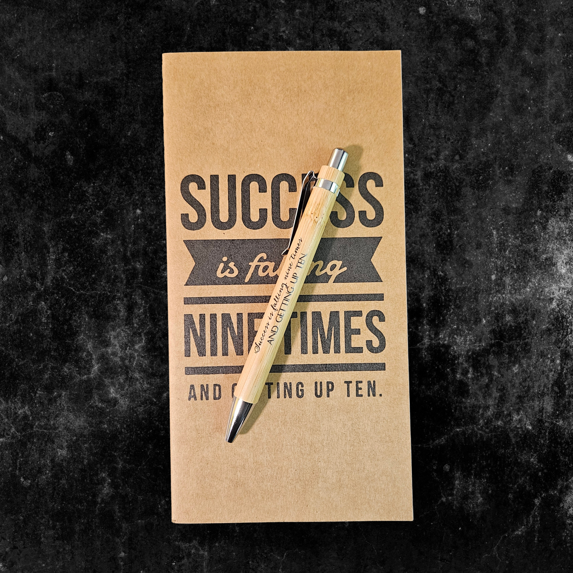 Kraft planner with motivational quote, Success is falling nine times and getting up ten, and pen on a dark textured background