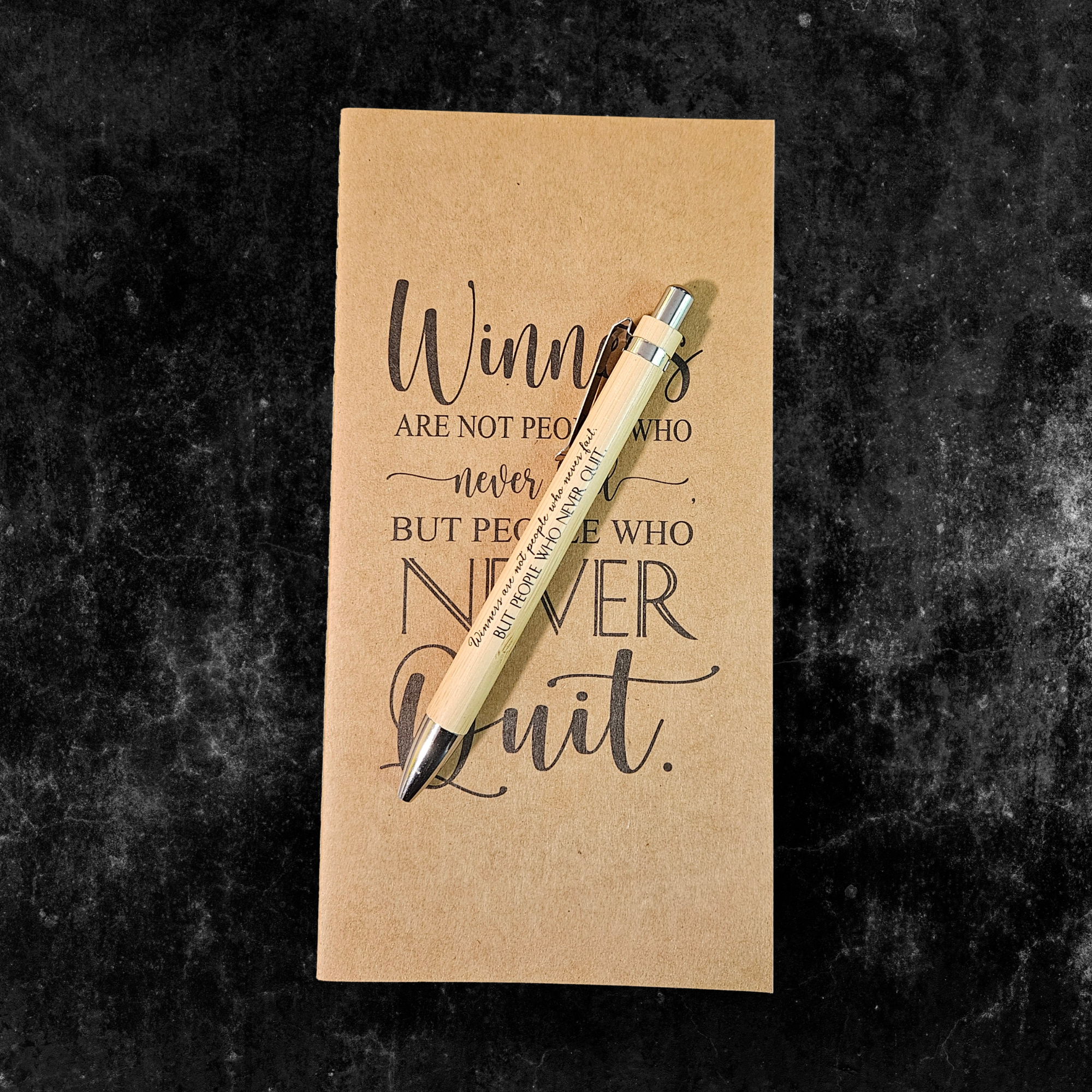 Kraft planner with motivational quote, Winners are not people who never fail but people who never quit, and pen on a dark textured background