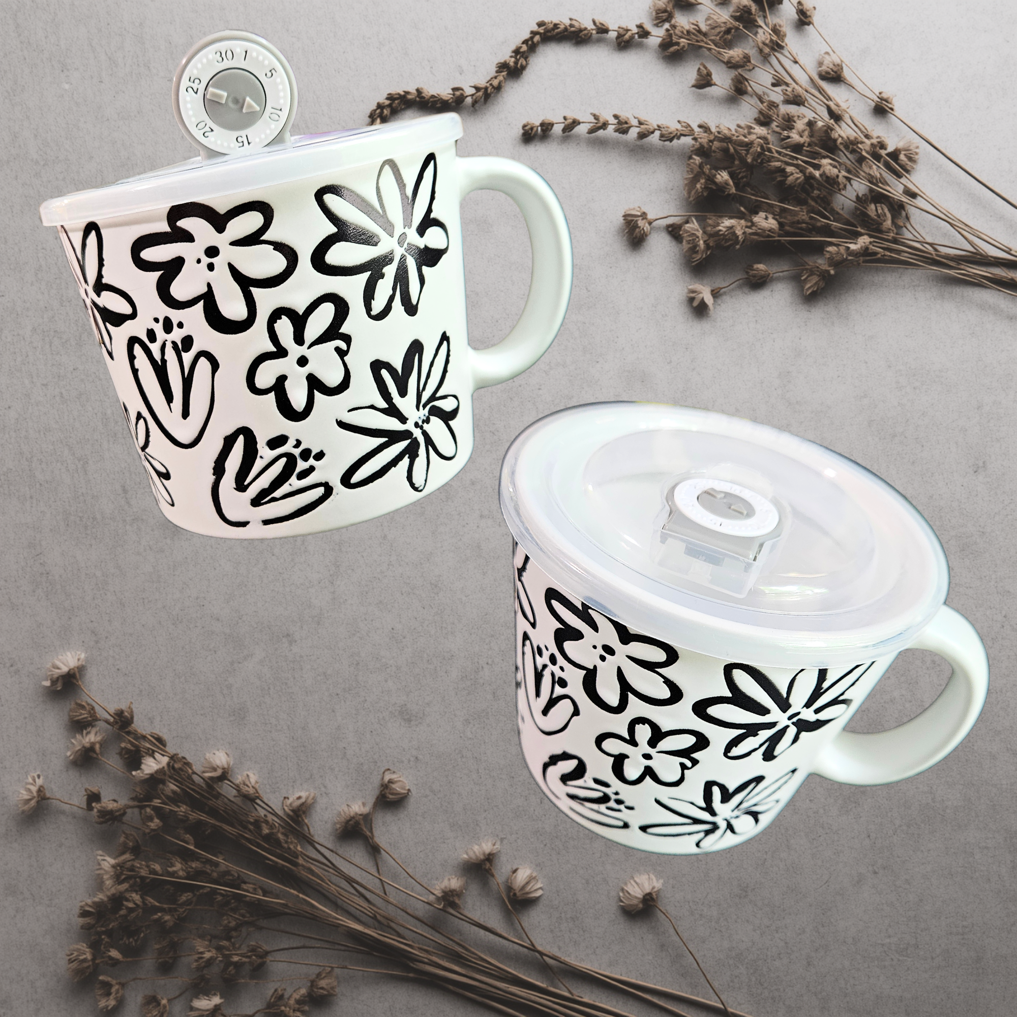 A ceramic soup mug with a modern floral design and a silicone‑sealed plastic lid featuring an adjustable dial and venting hole, available in black with white flowers or white with black flowers.